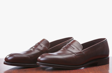 Footwear Concepts. Closeup of Pair of Stylish Brown Penny Loafer Shoes Against White. Placed on Wooden Reflecting Surface