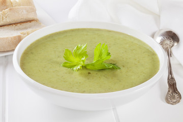 A bowl of creamy celery soup with a garnish of celery leaves, served with crusty bread.