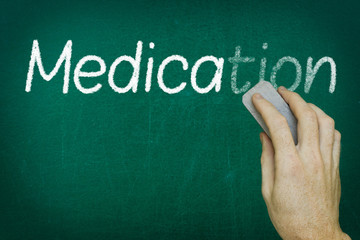 Hand erasing the word MEDICATION written on blackboard