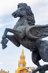 Fototapeta na wymiar View of a pegasus statue with the Clock Tower Gate in the background in Cartagena, Colombia.