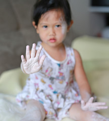 Cute little baby girl applying baby powder on her face and hand.