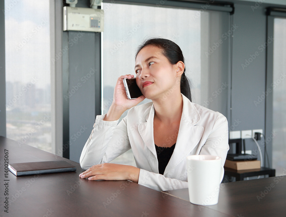 Wall mural young businesswoman sitting at the table on workplace in office using the telephone