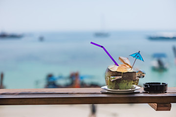 A coconut with straw for drinking at the beachfront with bluse sky background