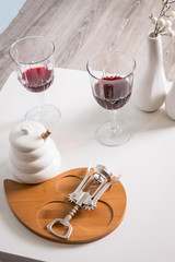 Red wine , wine glass, corkscrew. View from above over white wooden table background. wooden plate and two modern vases. modern decoration. 