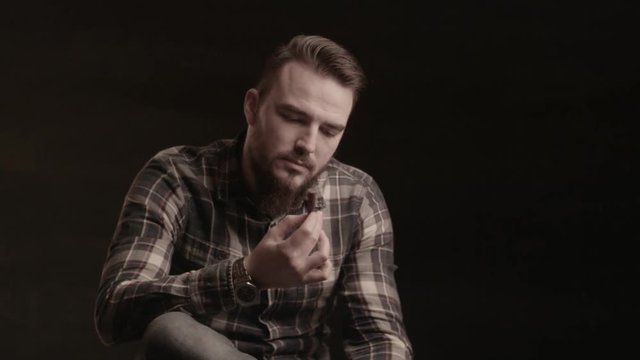 A man with a beard looking and smelling cigar in the studio on a black background