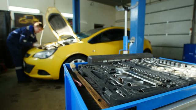 Worker works in professional car workshop near yellow car, time-lapse