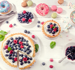 Sweet desserts with fresh berries on a white wooden table.