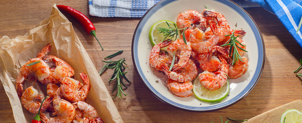 Shrimps on plate with lime, chili and rosemary on a wooden background.