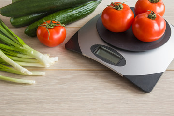 Red, big tomatoes on the weighing scales on the table with fresh cucumbers in the kitchen. Healthy eating and lifestyle.