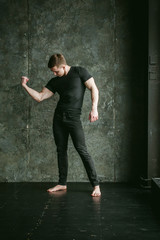 Fototapeta premium Young sexy men bodybuilder athlete, studio portrait loft on background of stylized Concrete brutal wall, guy model black Tshirt and trousers With powerful muscular arms demonstrates strength