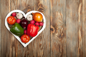 Vegetables. Peppers, tomatoes, garlic, onions, and radishes in the heart on rustic background
