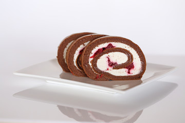 Chocolate roll with raspberries and vanilla cream on a white plate with reflection