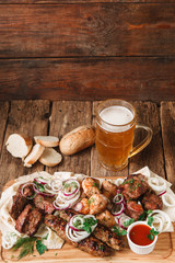 Appetizing meal in pub with fresh grilled meat assortment, pita bread, buns, and mug of cold light beer served on rustic wooden background, free space