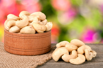 cashew nuts in a wooden bowl on the board with blurred garden background