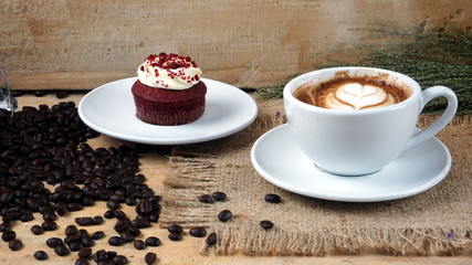 Cappuccino coffee and sweet chocolate red well wet cake. A cup of latte, cappuccino or espresso coffee with milk put on a wood table with dark roasting coffee beans. Drawing the foam milk on top.