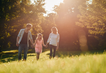 Happy young family holding hands while walking through a park