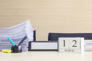 Closeup white wooden calendar with black 12 march word on blurred brown wood desk and wood wall textured background in office room view with copy space , selective focus at the calendar