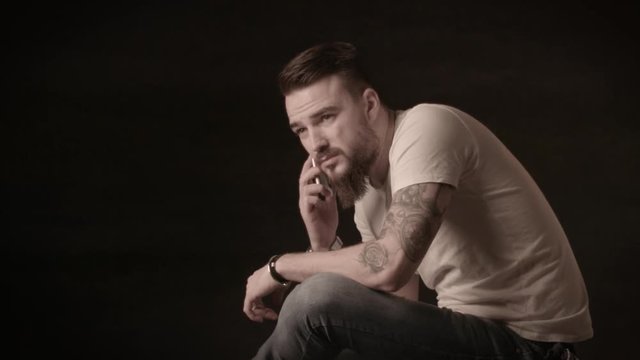 Handsome man with a beard talking on the phone in a studio on a black background