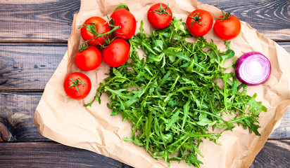 Organic vegetables: cherry tomatoes, mozzarella cheese, rocket, red onion on parchment over dark rustic wooden table. Traditional italian salad ingredients. Mediterranean food. Top view. 
