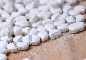 Macro of the white pills cut into pieces on wooden brown background.