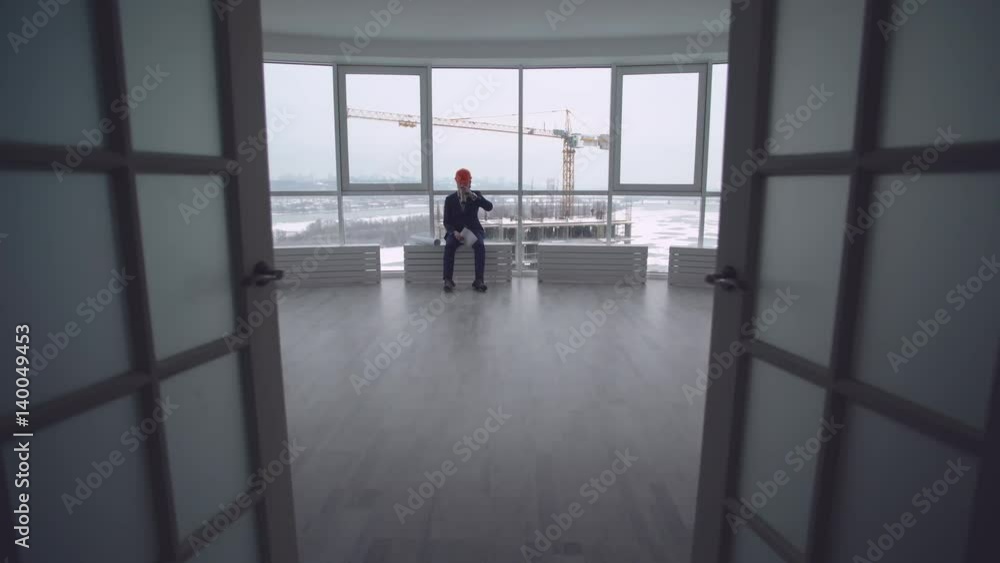 Poster tired handsome architect has a break resting drinking coffee. Manager of building engineer sitting in the modern office real estate company. Handsome man wearing in elegant suit and orange hard hat.