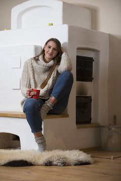Woman sitting at fire place, drinking cup of tea