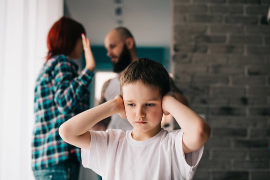 Sad child covering his ears with hands during parents quarrel.