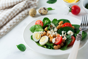 Vegetarian salad with spinach, chickpeas, cherry tomatoes, egg and Feta cheese and lemon on a light background. Selective focus.