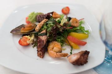 Salad with seafood, octopus, strawberry, citrus and greens into the white plate