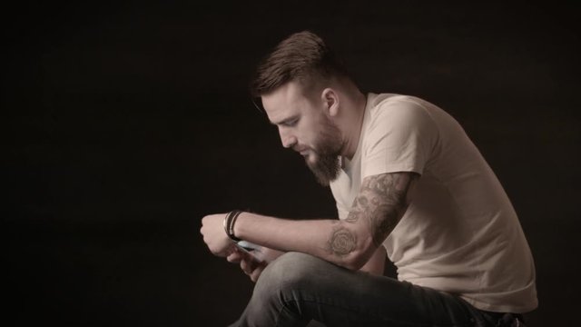 Handsome man with a beard writes messages on the phone in a studio on a black background