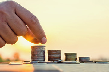 Hand putting coin on coins stack with Concept,Saving money and nature sunset background