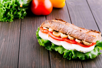 Sandwich of wholemeal bread and vegetables lies on dark wooden table