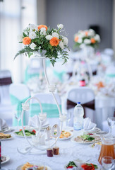 Curvy steel vase with roses and orange flowers stands in the middle of round dinner table