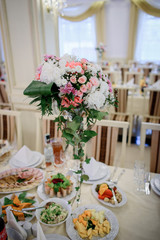 Tall vase with bouquet of white roses and greenery stands on dinner table