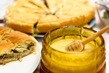 Honey in a glass dish on a table and pie on the background
