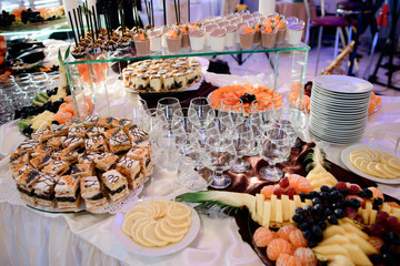 Dishes with sweets and fruits stand on table with empty glassware