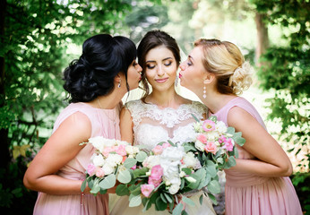 Bridesmaids lean to pretty bride holding white bouquets in their hands