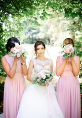 Bridesmaids in pink dresses hide their faces posing with bride in forest