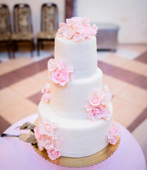 White wedding cake decorated with pink roses and white glaze