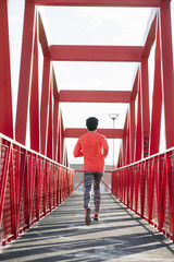 Young boy running down the red bridge, back
