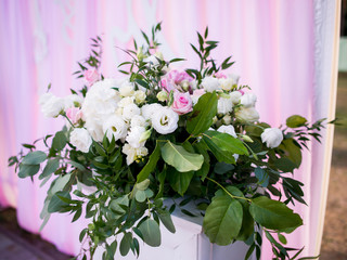 Rich bouquet of roses and greenery stand on pillar before wedding altar