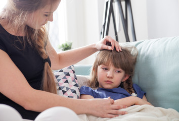 Sick little girl lying in bed mother checking her temperature