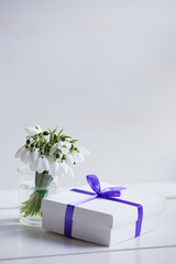 Beautiful white snowdrops with gift box on white wooden background