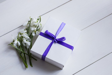 Beautiful white snowdrops with gift box on white wooden background