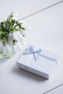 Beautiful white snowdrops with gift box on white wooden background