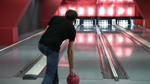 Man is playing bowling slow motion. The young man knocks out the strike. Guy will beat 10 points.