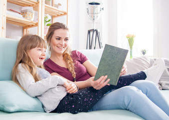 Mother and daughter sitting on sofa and reading book together