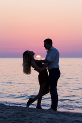 Dark silhouettes of dancing young couple on seaside at sunrise