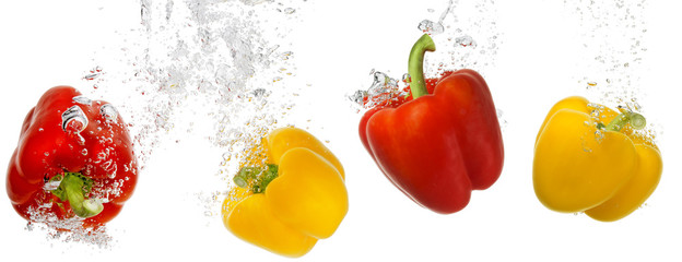 four bell peppers falling into water isolated on white background