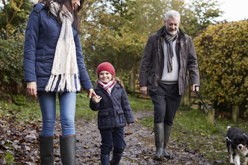 Multi Generation Family Take Dog For Walk In Fall Landscape